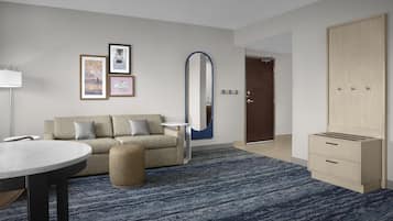 A modern hotel room with a sofa, a round table, a mirror, and a wardrobe.