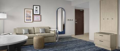Una habitación de hotel moderna con sofá, una mesa redonda, un espejo y un armario.
