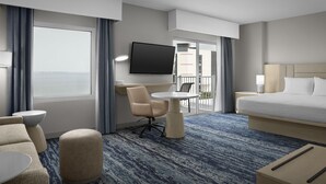 A hotel room with a bed, a desk, a chair, a TV, and a view of the outside.