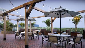 An outdoor patio with brick flooring, wooden pergola, and tables with chairs.