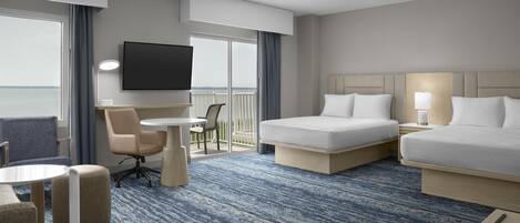 A hotel room with two beds, a TV, a desk, and a balcony with a view.