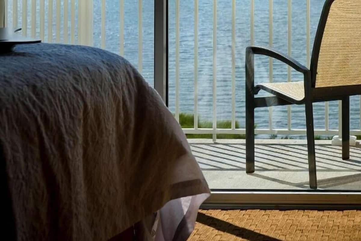 A room with a large window overlooking a body of water, a bed, and a chair.