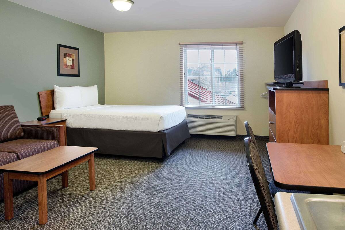 A hotel room with a bed, a desk, a chair, a television, and a window with blinds.