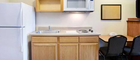 A compact kitchenette with a microwave, a refrigerator, a sink, and a small dining area with two chairs.