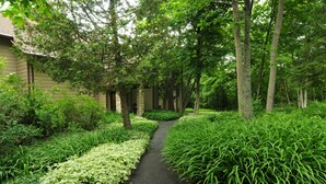 A pathway flanked by lush greenery and trees, leading to a building with a stone facade. - The Inn at Little Sister Hill (Sister Bay)
