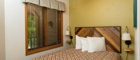 A bedroom with a bed, a ceiling fan, a window with blinds, and a wall-mounted lamp.