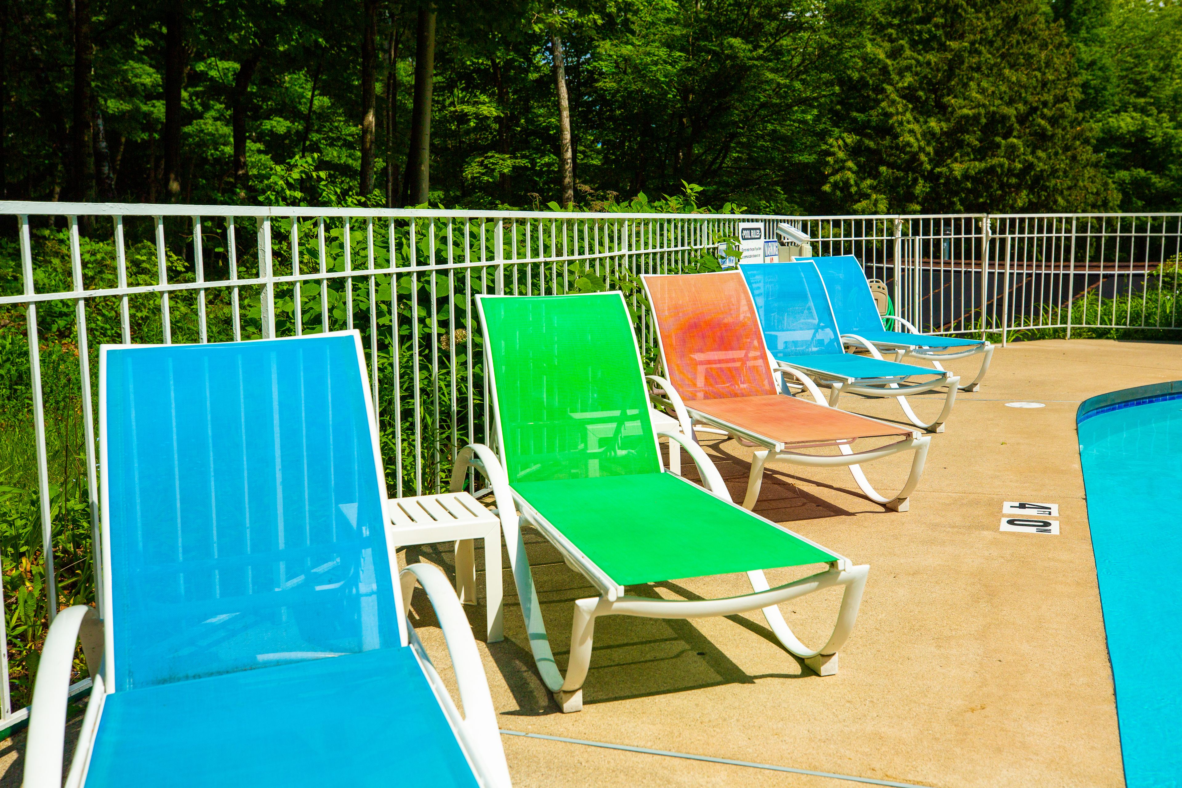 Un área junto a la piscina con sillones de descanso y una cerca.