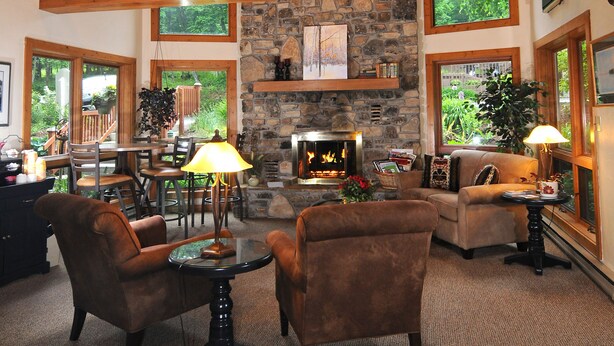 A spacious living room with a stone fireplace, wooden beams, and large windows offering views of greenery. - The Inn at Little Sister Hill (Sister Bay)