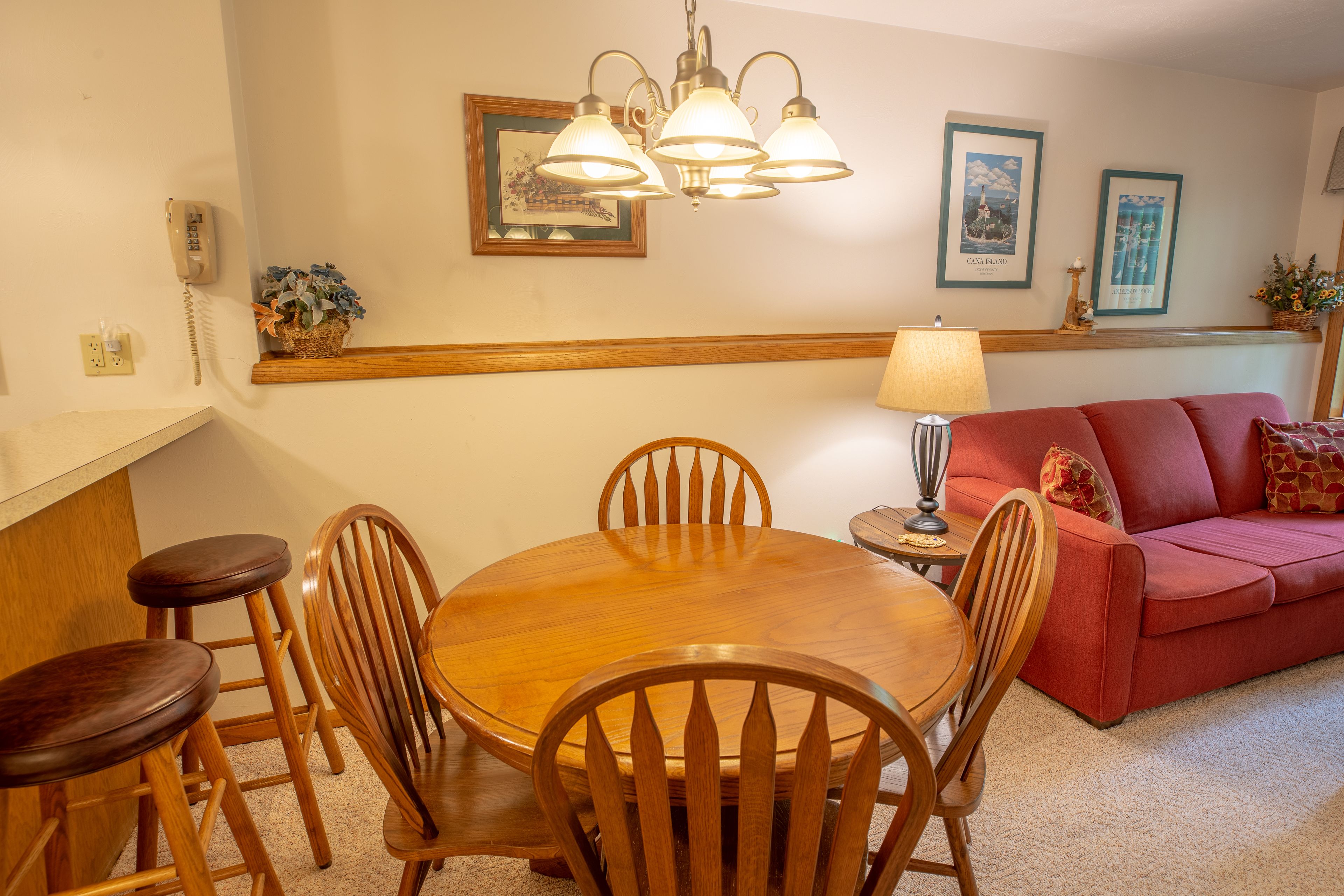 A dining area with a wooden table and chairs, a red sofa, and wall-mounted light fixtures.