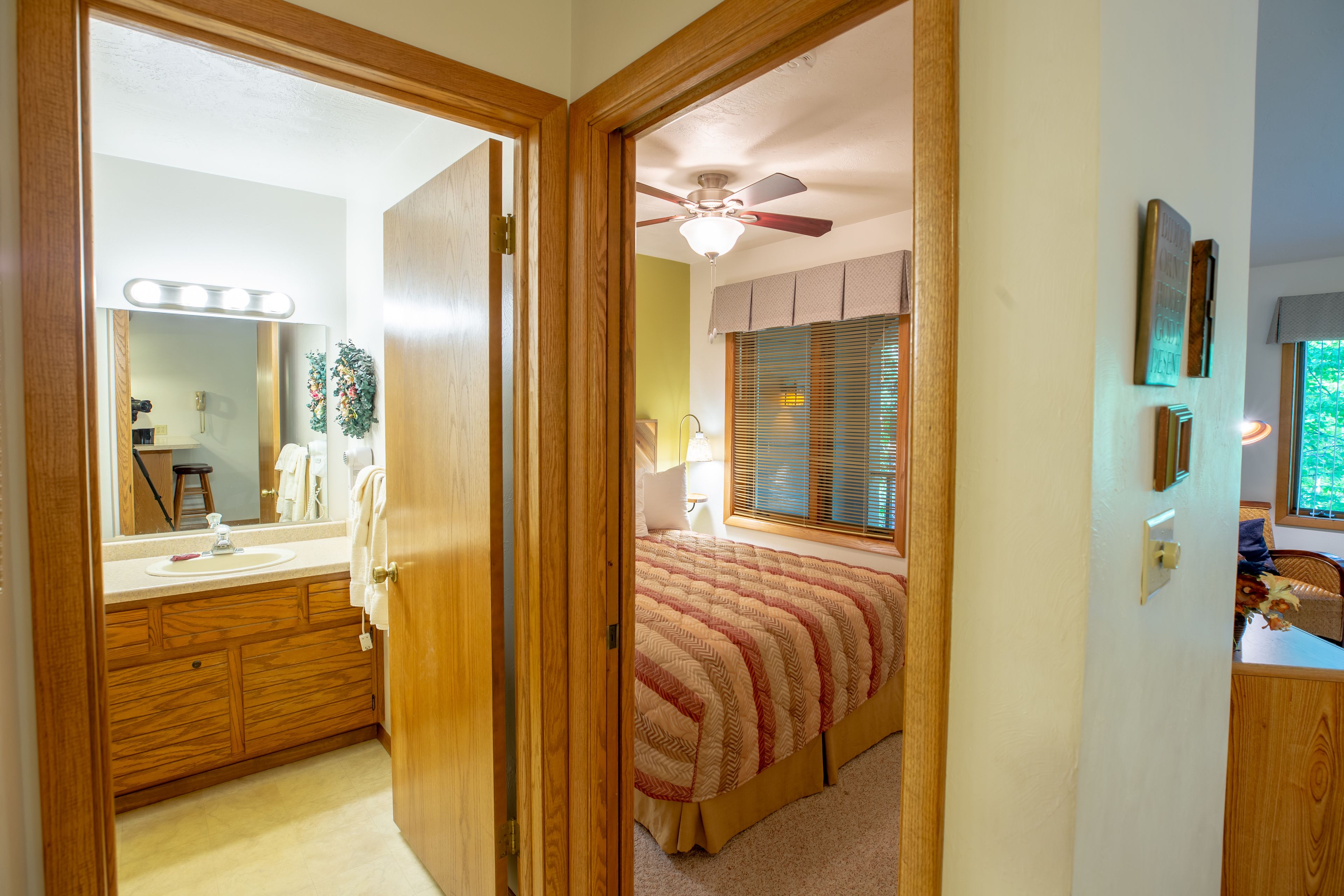 Une chambre à coucher comprenant un lit, un ventilateur de plafond, une fenêtre avec des stores, une table de chevet et une commode.