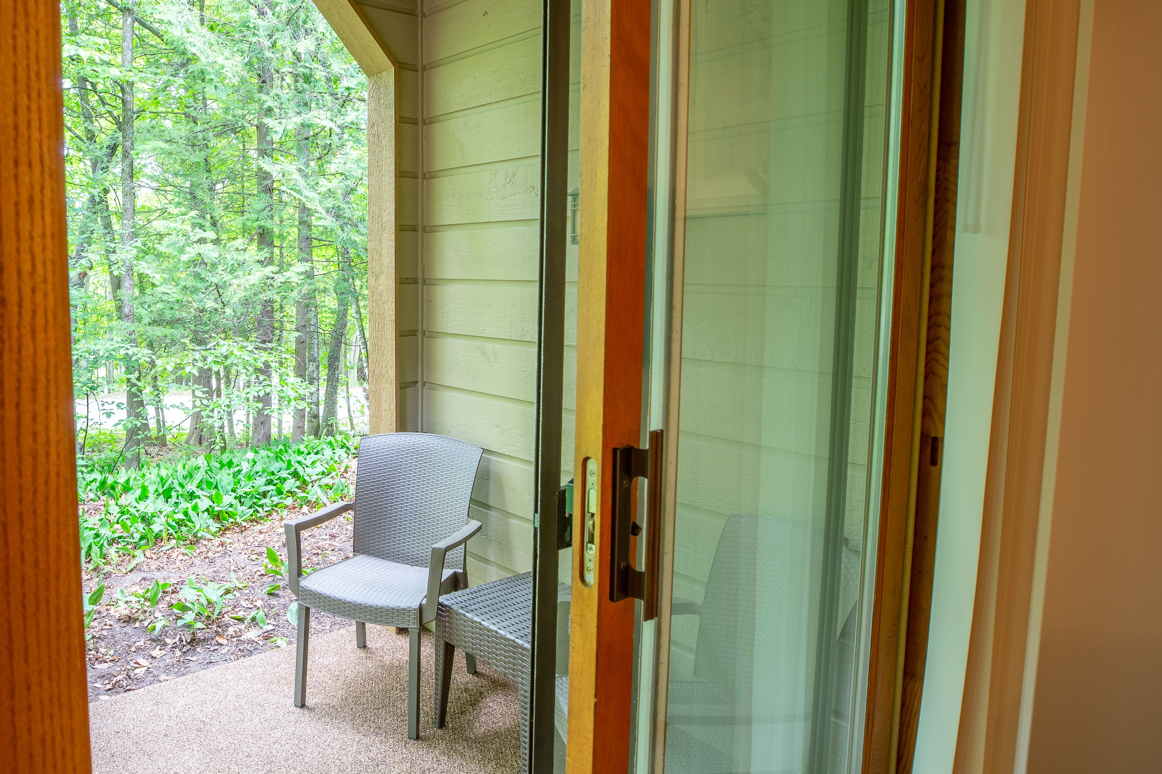 Una habitación con puerta de vidrio corrediza que da a un espacio exterior cubierto con una silla y vistas a un bosque.