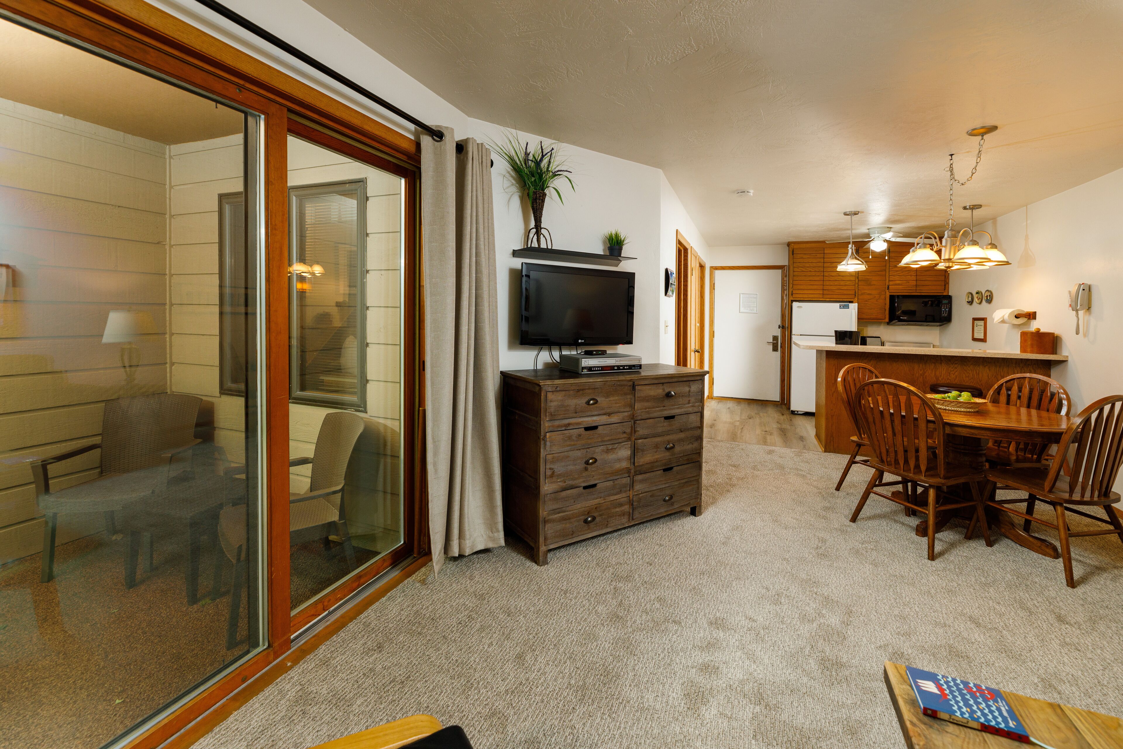 A modern kitchen with a dining area, a TV, and a sliding glass door leading to a balcony.