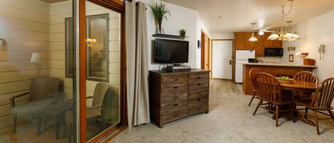 A modern kitchen with a dining area, a TV, and a sliding glass door leading to a balcony.