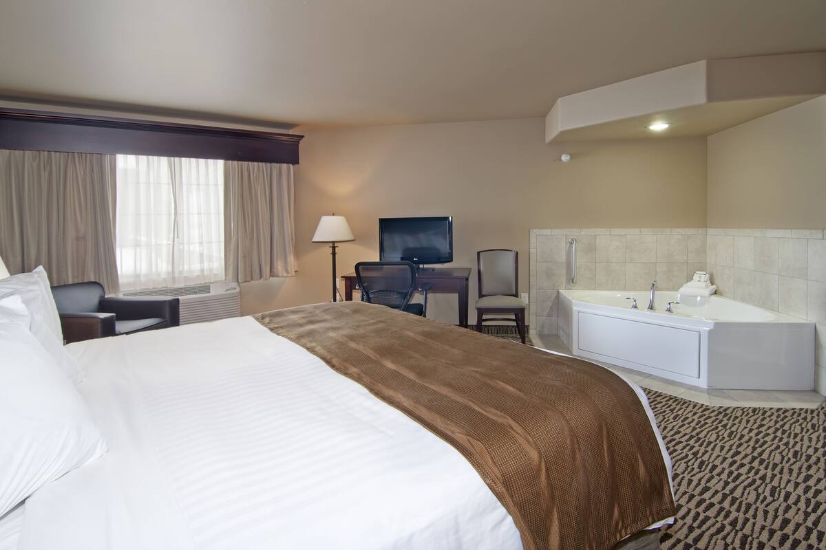 A hotel room with a large bed, a desk with a computer, a TV, and a separate bathroom with a bathtub.
