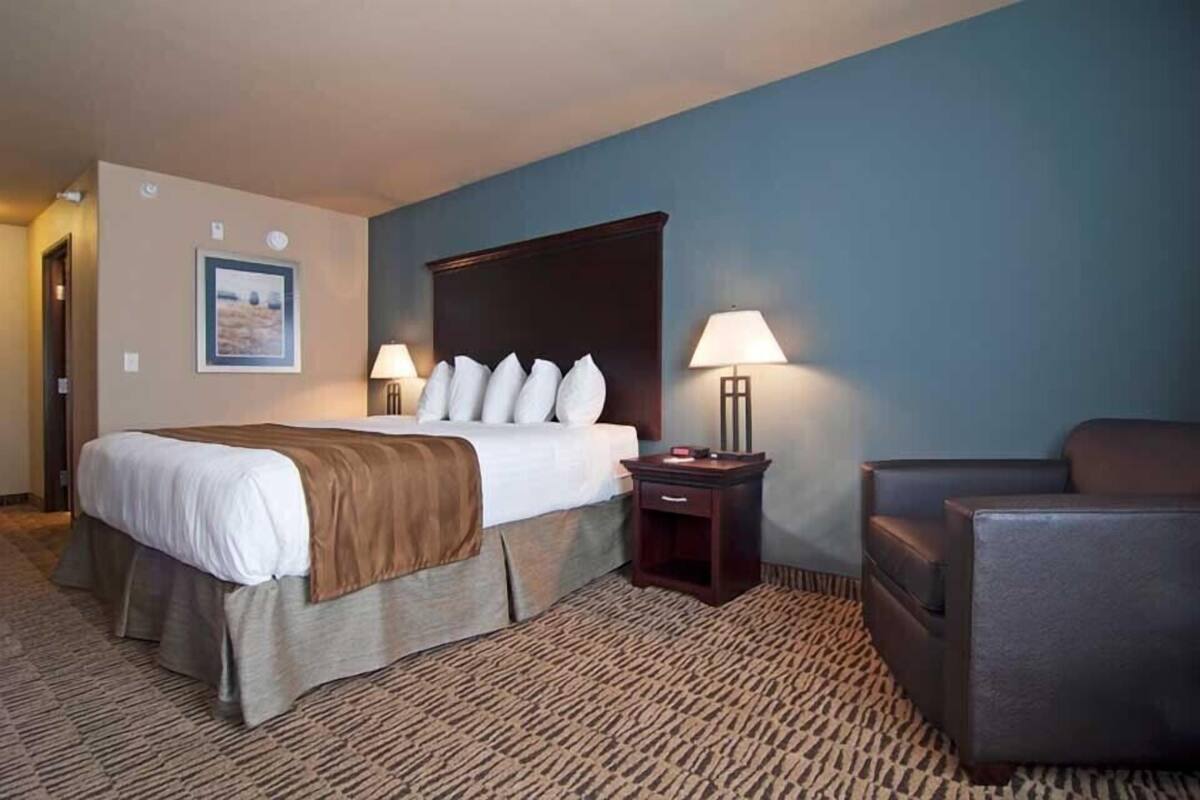 A hotel room with a large bed, two bedside lamps, a chair, and a framed picture on the wall.