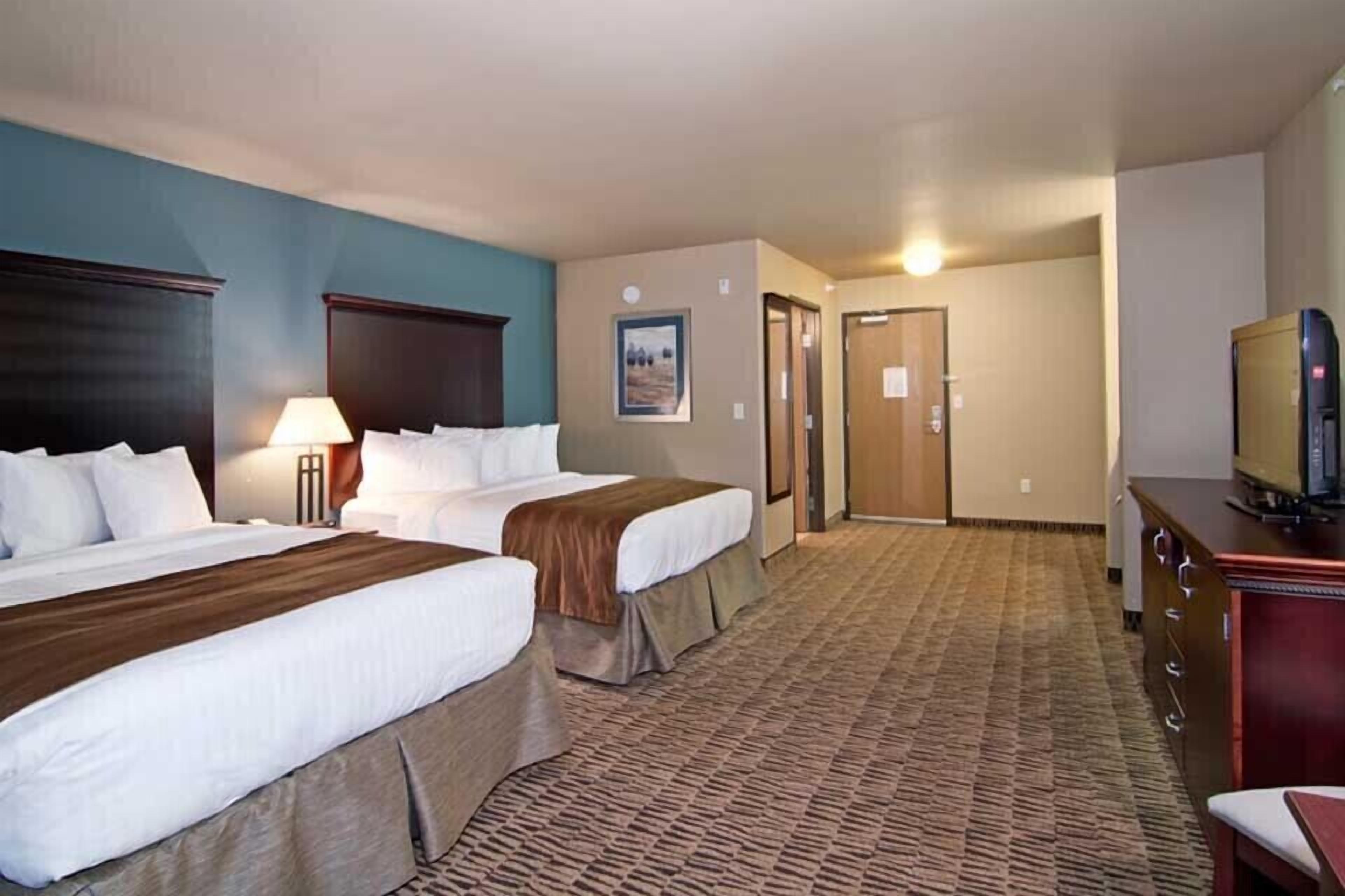 A hotel room with two beds, a desk, a television, and a carpeted floor.