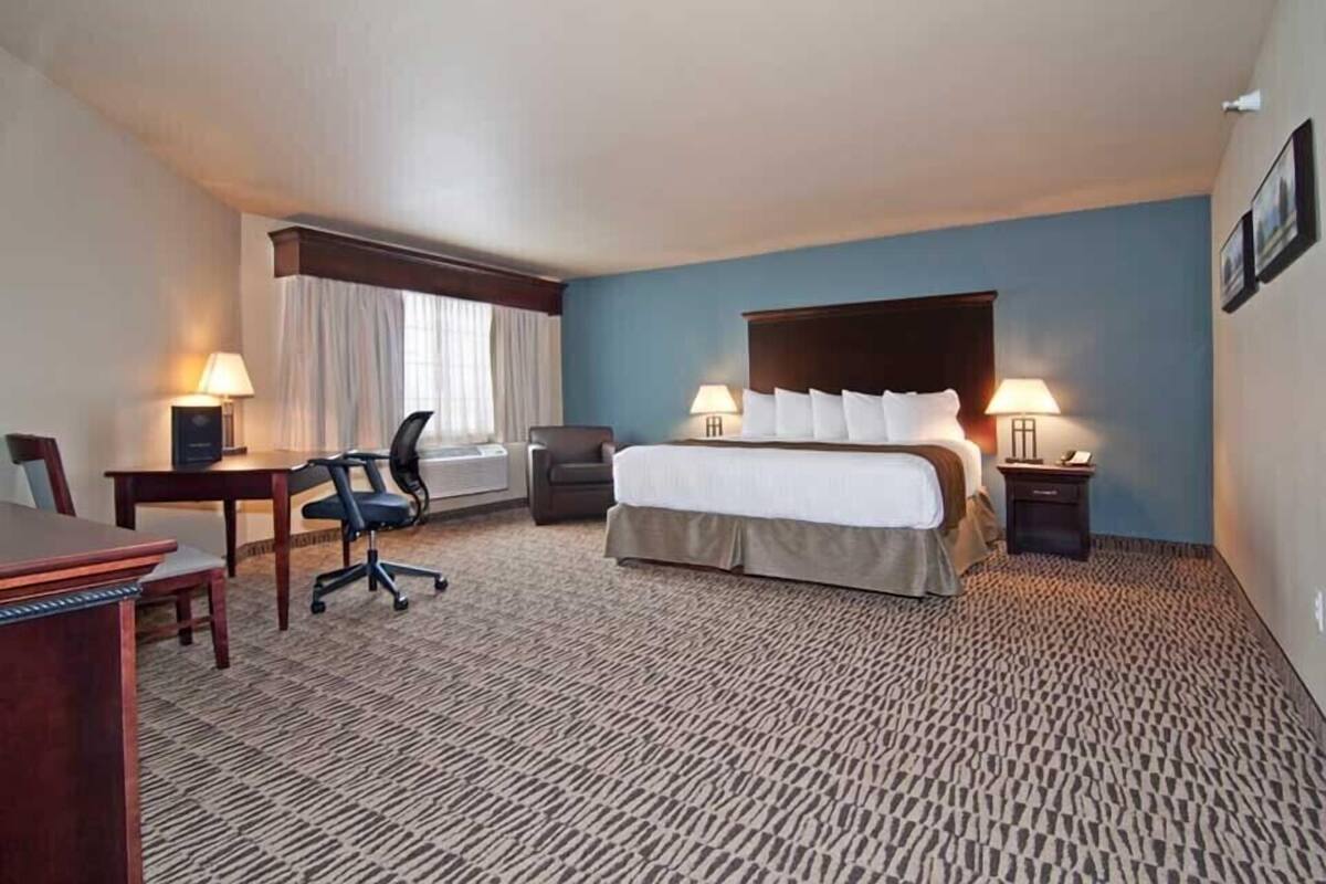 A hotel room with a bed, desk, chair, and two bedside lamps.