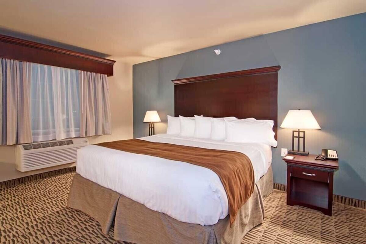 A hotel room with a large bed, two bedside lamps, a nightstand, and a window with curtains.