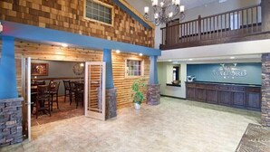 A spacious lobby with a wooden wall, a reception desk, and a staircase leading to an upper level. - The Watford (Watford City)
