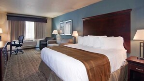 A hotel room with a large bed, a desk, a chair, and a window with curtains. - The Watford (Watford City)