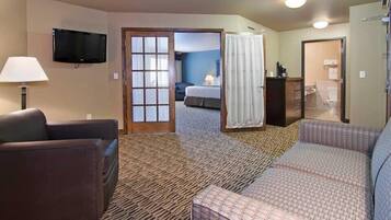 A hotel room with a sofa, a TV, a bed, and a bathroom visible through an open door.