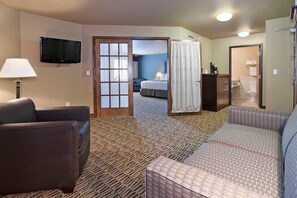 A hotel room with a sofa, a TV, a bed, and a bathroom visible through an open door. - The Watford (Watford City)