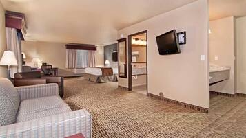 A hotel room with a sofa, a small table, a TV mounted on the wall, and a bed.