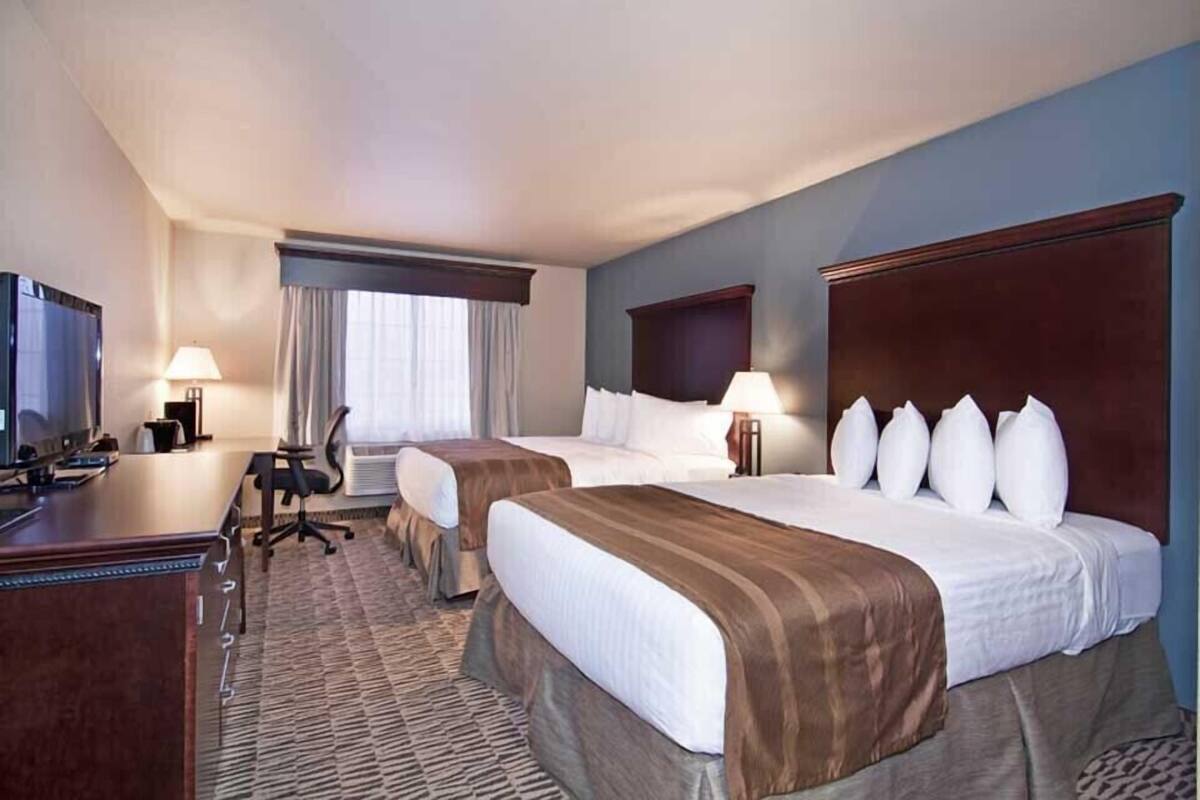 A hotel room with two beds, a desk, a television, and a window with curtains.
