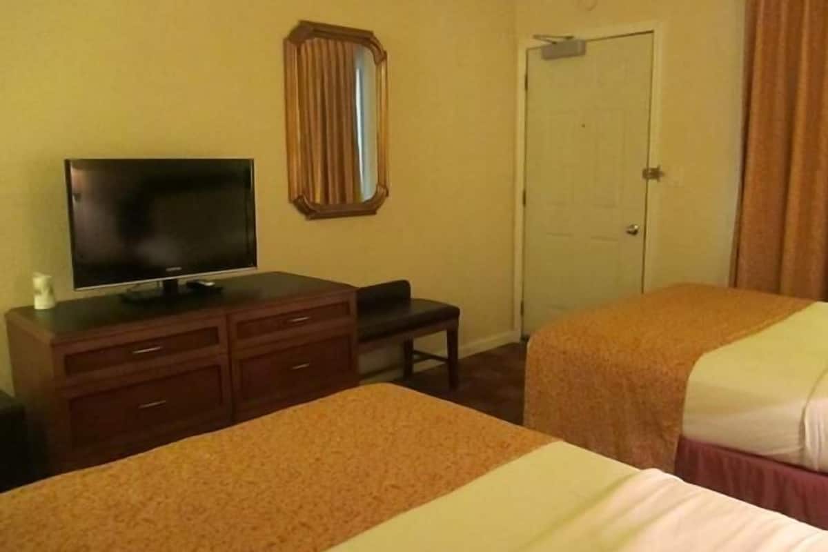 A hotel room with two beds, a TV on a wooden dresser, a mirror, and a door.
