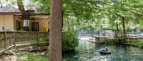 A serene riverside scene with a wooden bridge, a boat, and a building with a sloped roof.