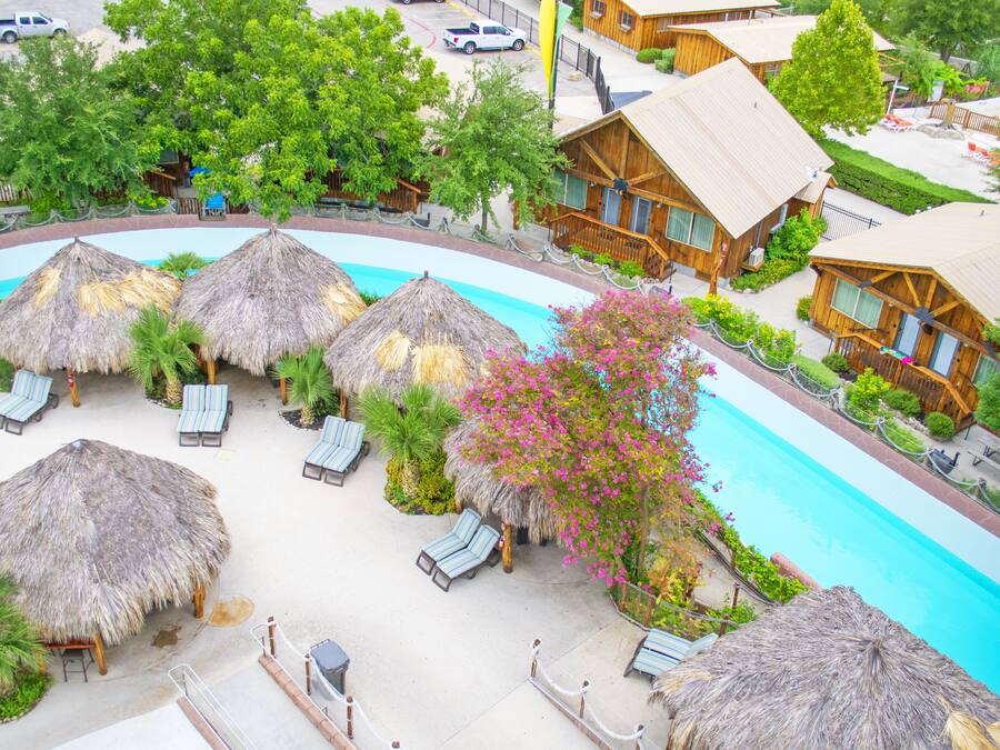 Un complejo turístico con piscina, sombrillas de paja y cabañas de madera.