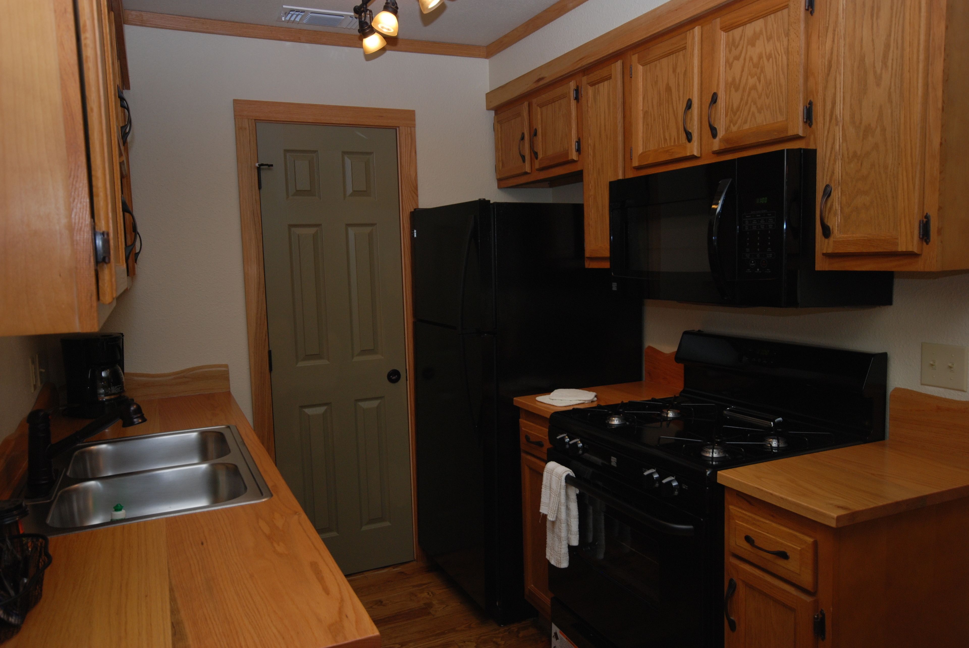 A kitchen with wooden cabinets, a black refrigerator, a stove, and a sink.