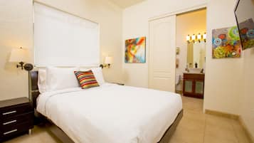 Une chambre d’hôtel comprenant un lit, des tables de chevet, une lampe, un tableau, une salle de bain avec un miroir et un lavabo.