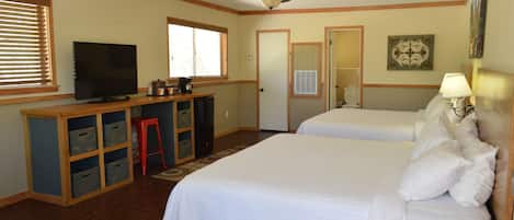 Een hotelkamer met twee bedden, een bureau met een televisie, een plafondventilator en een raam met jaloezieën.