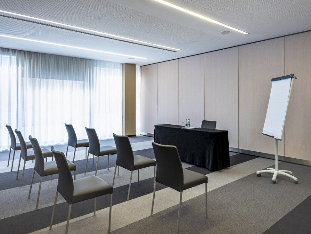 Un salón de conferencias con una mesa, sillas, una pizarra y un amplio ventanal con cortinas.