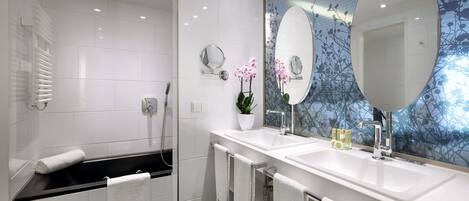 A modern bathroom with a bathtub, two sinks, and a large mirror.
