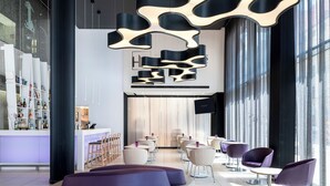 A modern hotel lobby with a curved seating area, a bar with a white countertop, and a large TV screen.