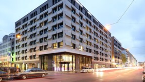 A modern hotel with a corner entrance, multiple floors, and a prominent glass facade.