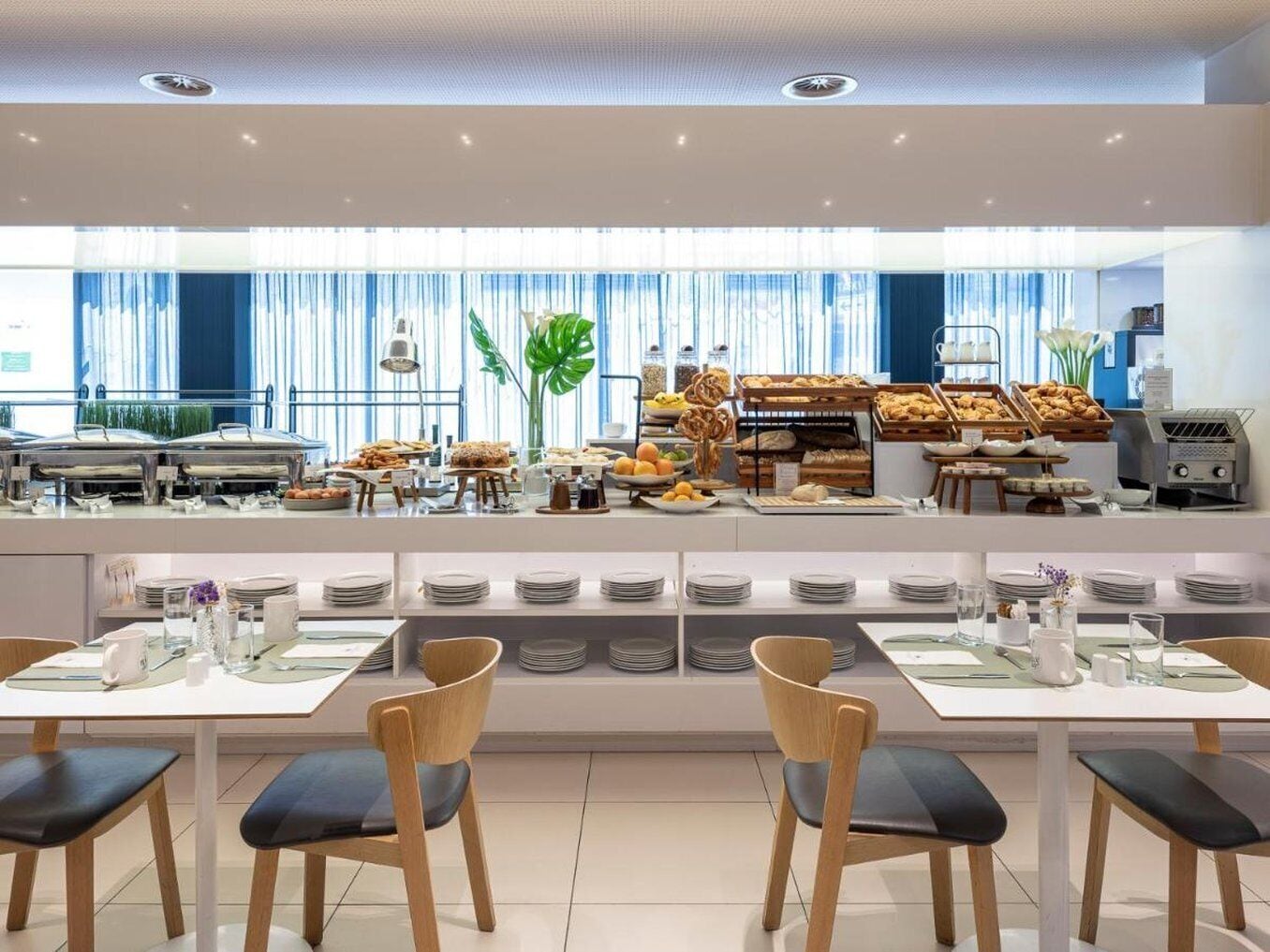 Un bufé de desayuno moderno con diversos alimentos y una zona de estar con mesas y sillas.