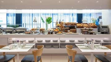Un bufé de desayuno moderno con diversos alimentos y una zona de estar con mesas y sillas.