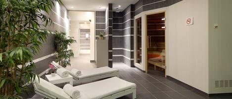 A modern spa area with two white massage tables, a bamboo plant, and a tiled wall with a black and white pattern.