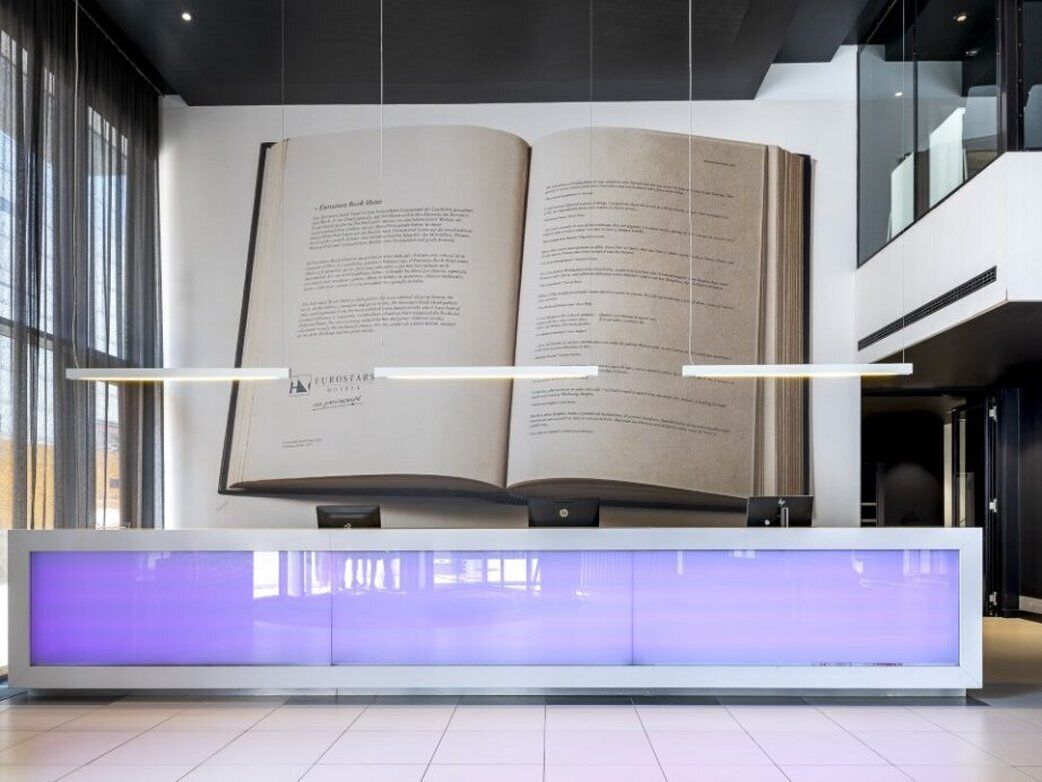 A reception desk with an open book on display, a modern reception area, and a glass partition.