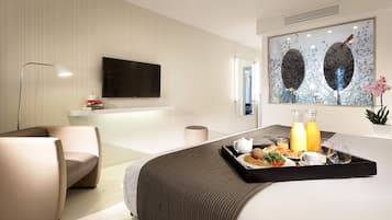 A modern hotel room with a bed, a bedside table with a tray of breakfast, a flat-screen TV, and a large window with a nature-themed artwork.
