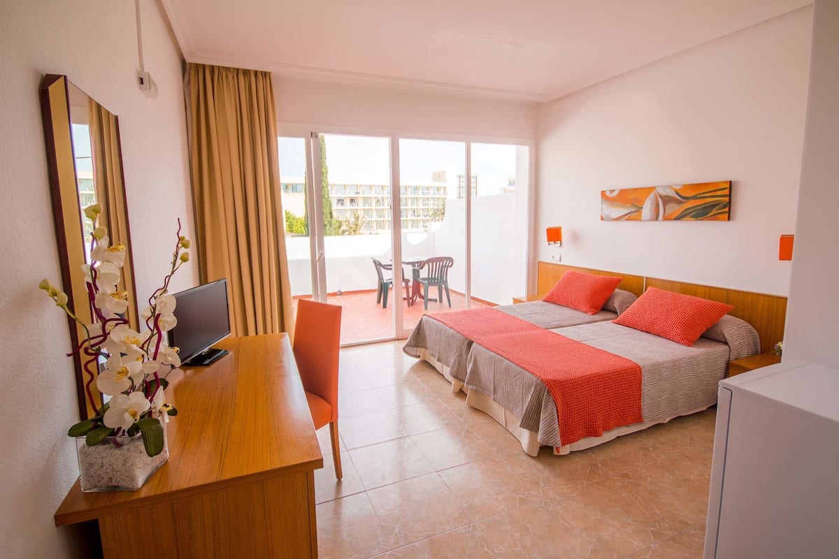 A hotel room with a bed, a desk with a computer, a chair, and a balcony with a table and chairs.