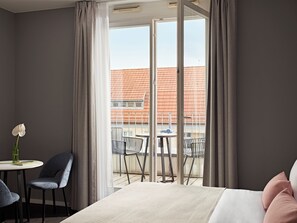 Une chambre d’hôtel comprenant un lit, un bureau avec une chaise et un balcon avec des chaises et une table.