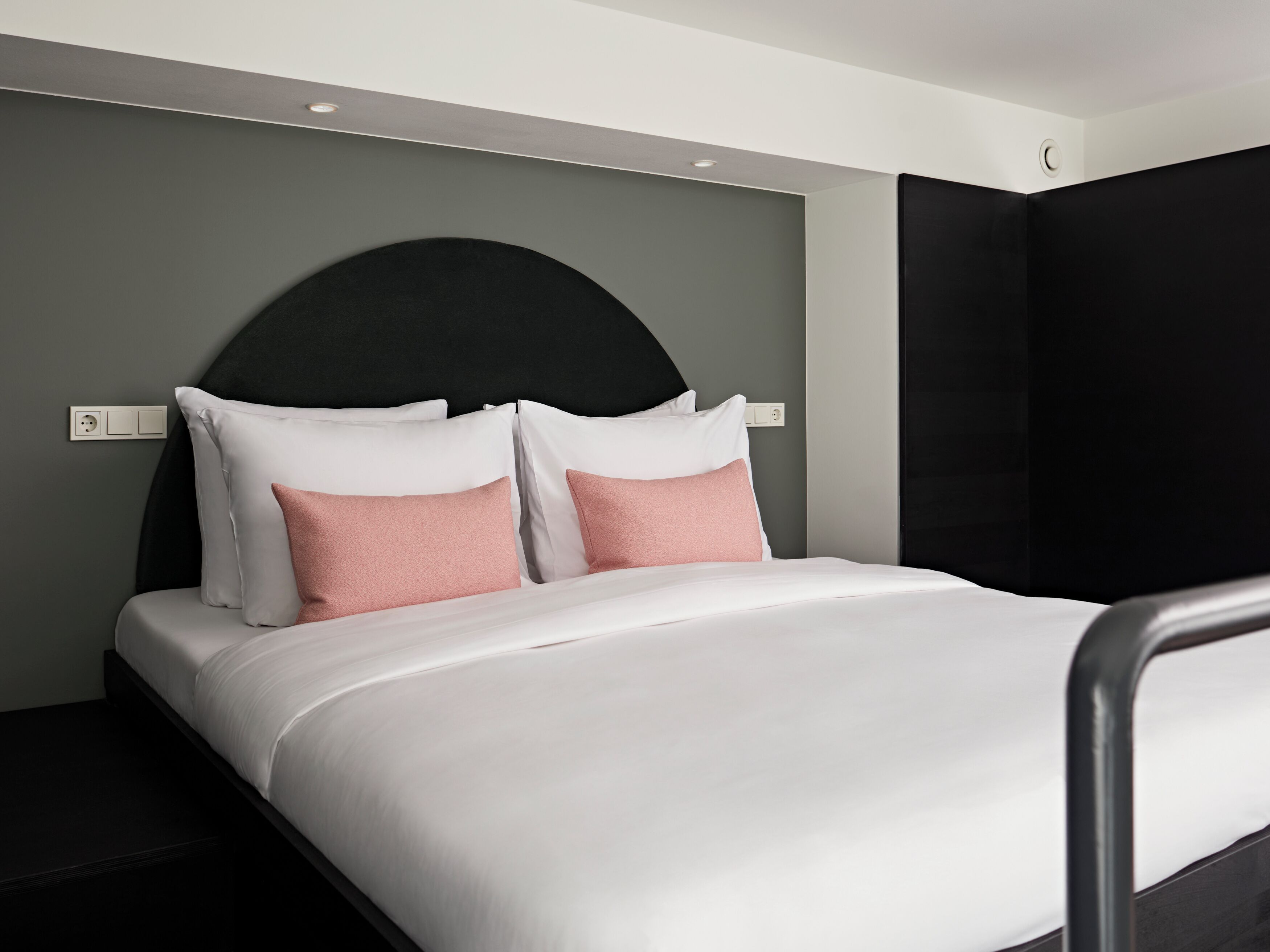 Ein modernes Hotelzimmer mit einem Bett, einem schwarzen Kopfteil und einer grauen Wand.
