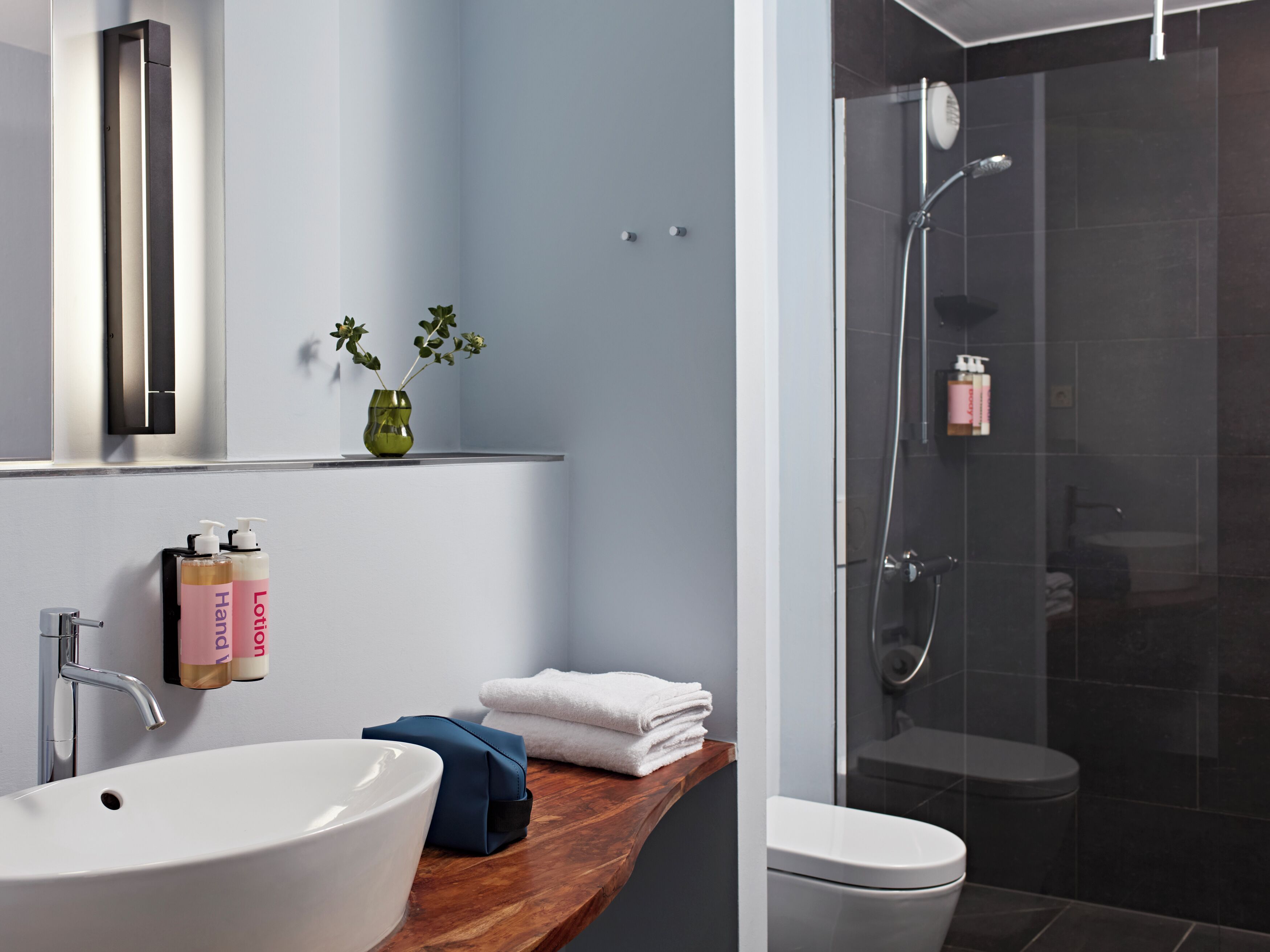 Un baño moderno con un lavamanos blanco, un mueble de tocador de madera, una cabina de ducha de vidrio y un inodoro.