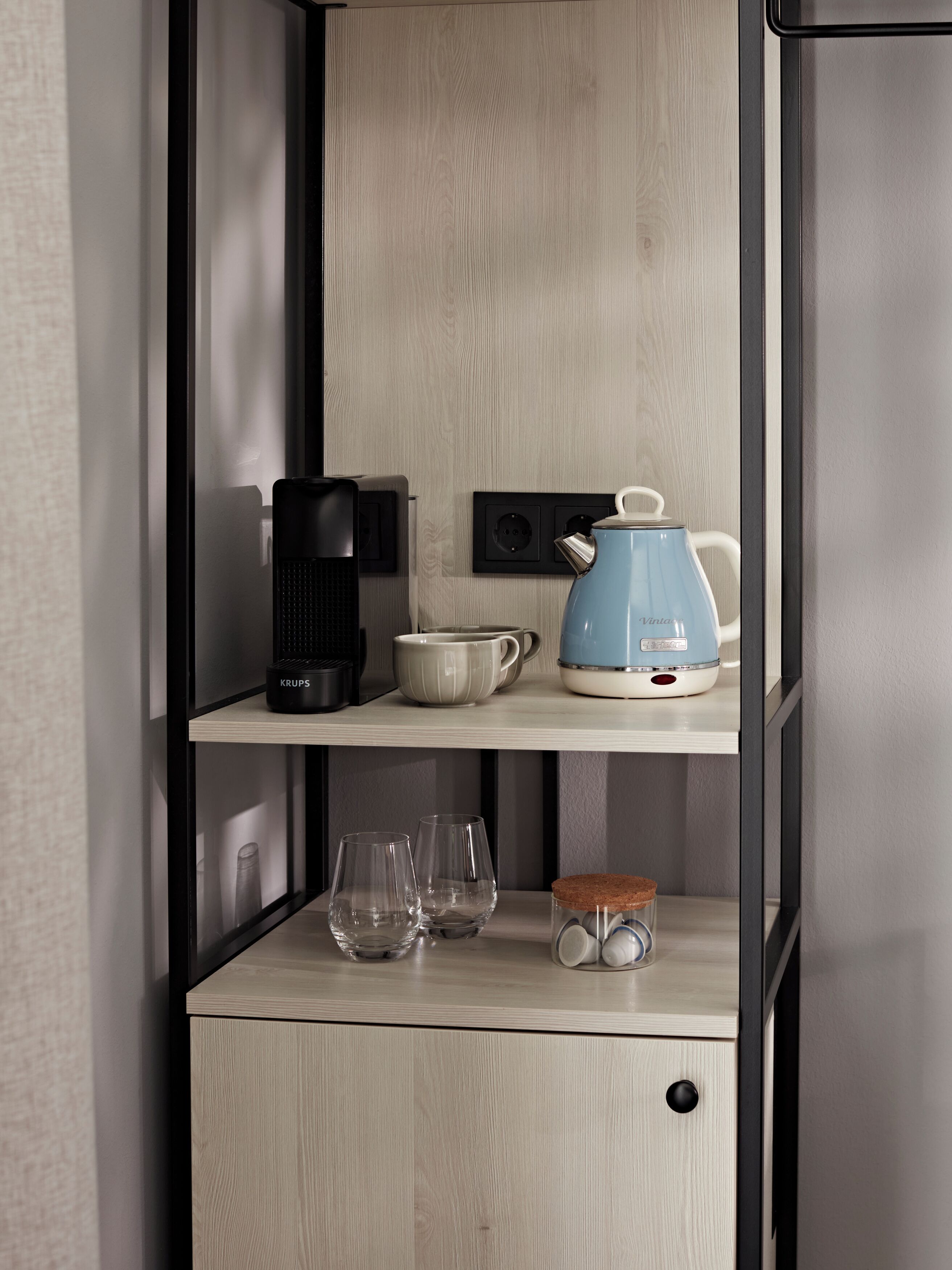 A kitchen with a wooden cabinet, a coffee maker, a kettle, and a glass set.