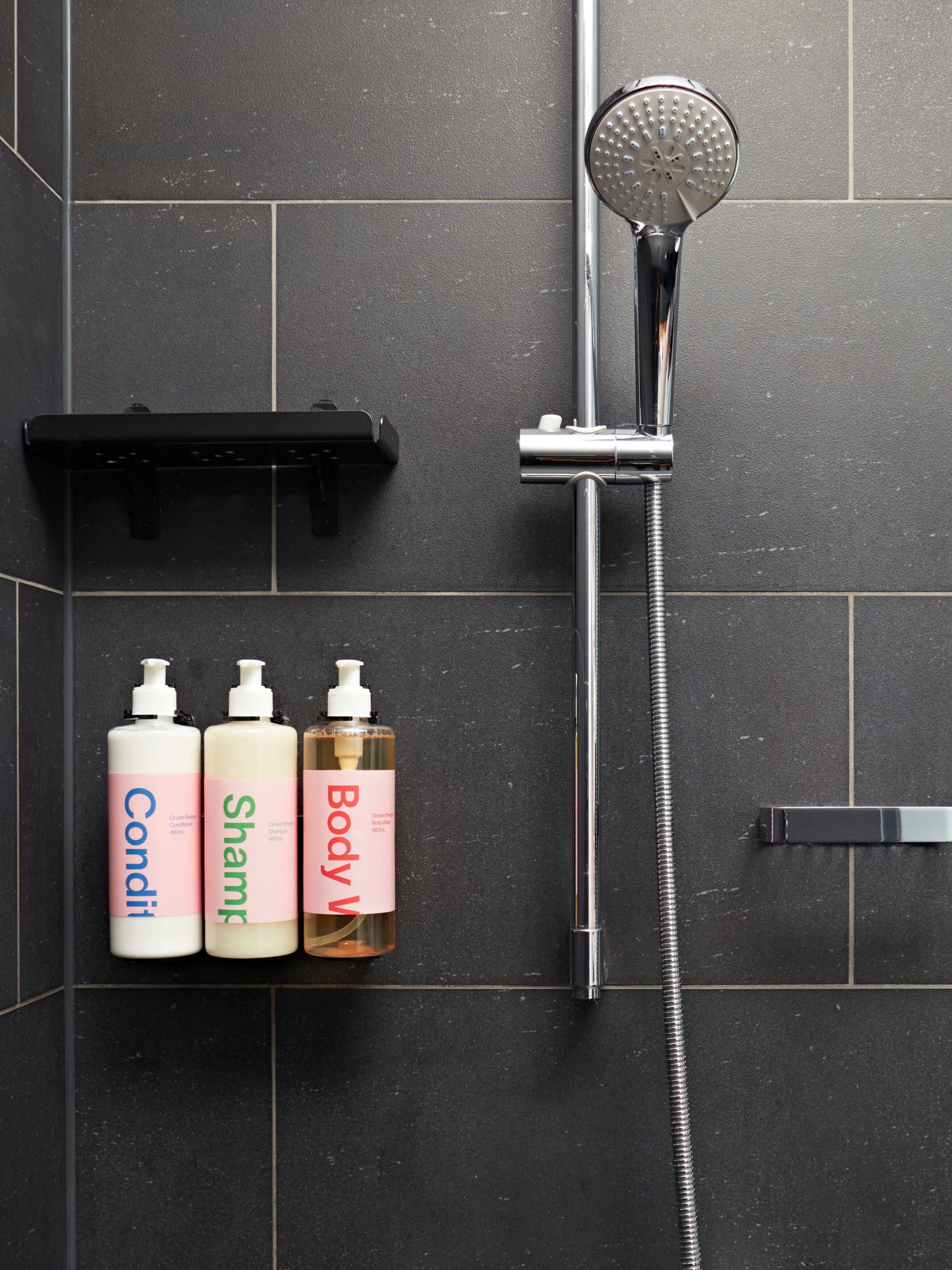 A bathroom with a shower, a black towel rack, and three bottles of body wash.