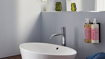 Un baño con un lavamanos blanco, un grifo moderno y dos botellas de loción en una estantería.